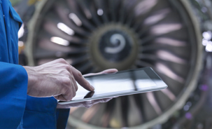 Aircraft engineer using a tablet with a commercial aircraft engine in the background.